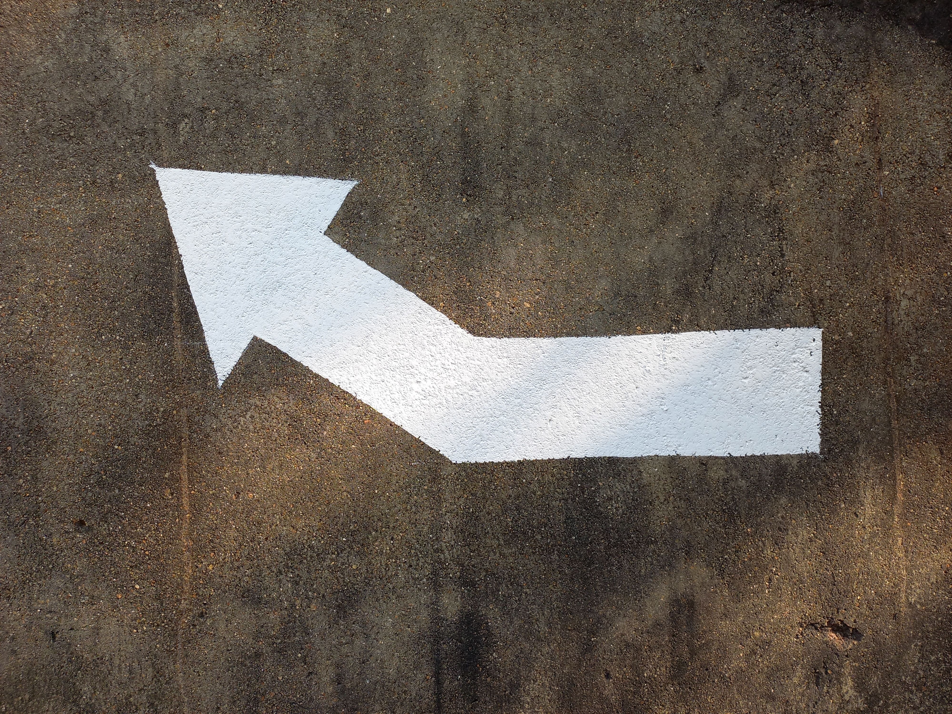 White painted arrow on concrete pavement indicating direction.