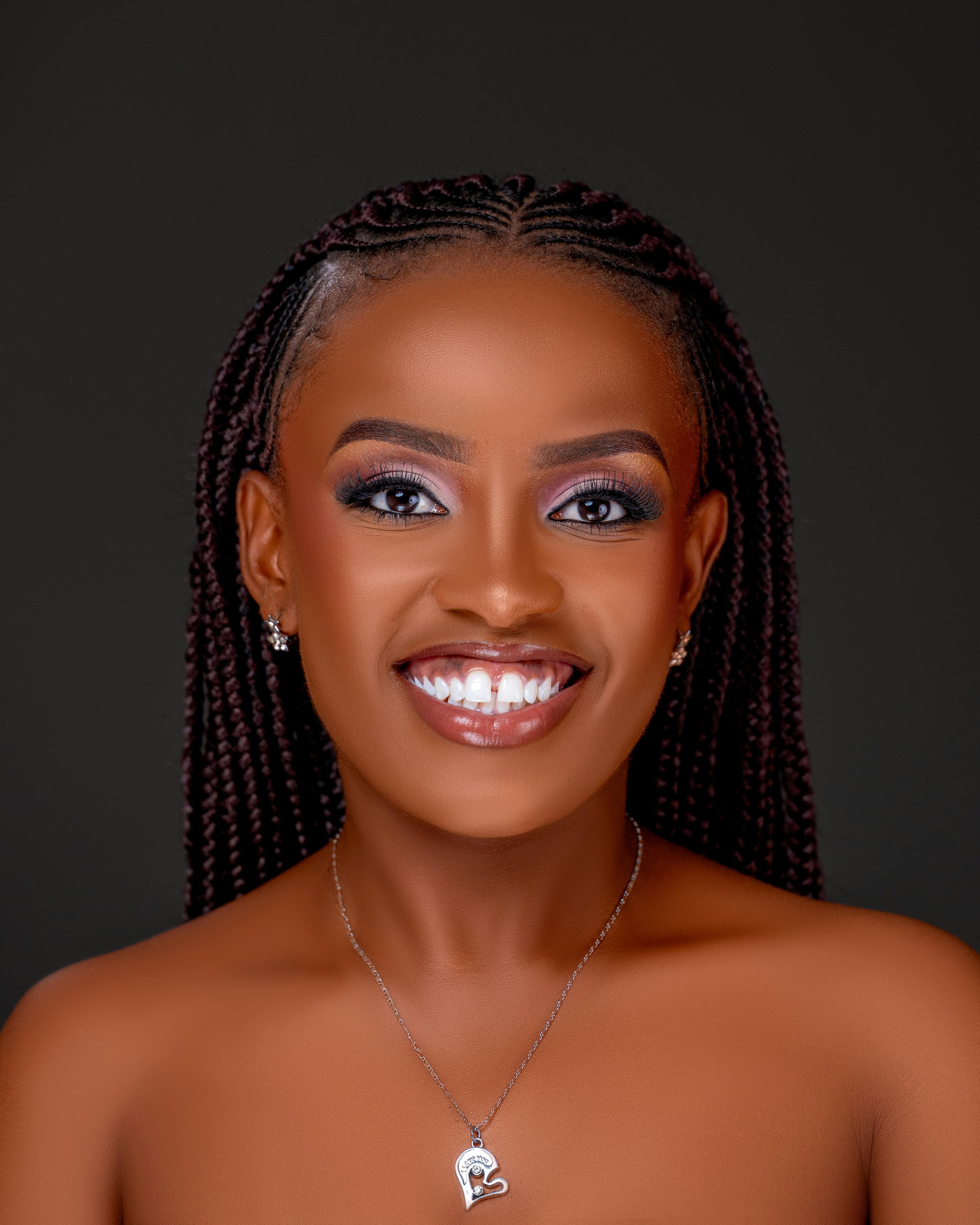 Close-up portrait of a smiling woman with braided hair and elegant jewelry on a dark background.