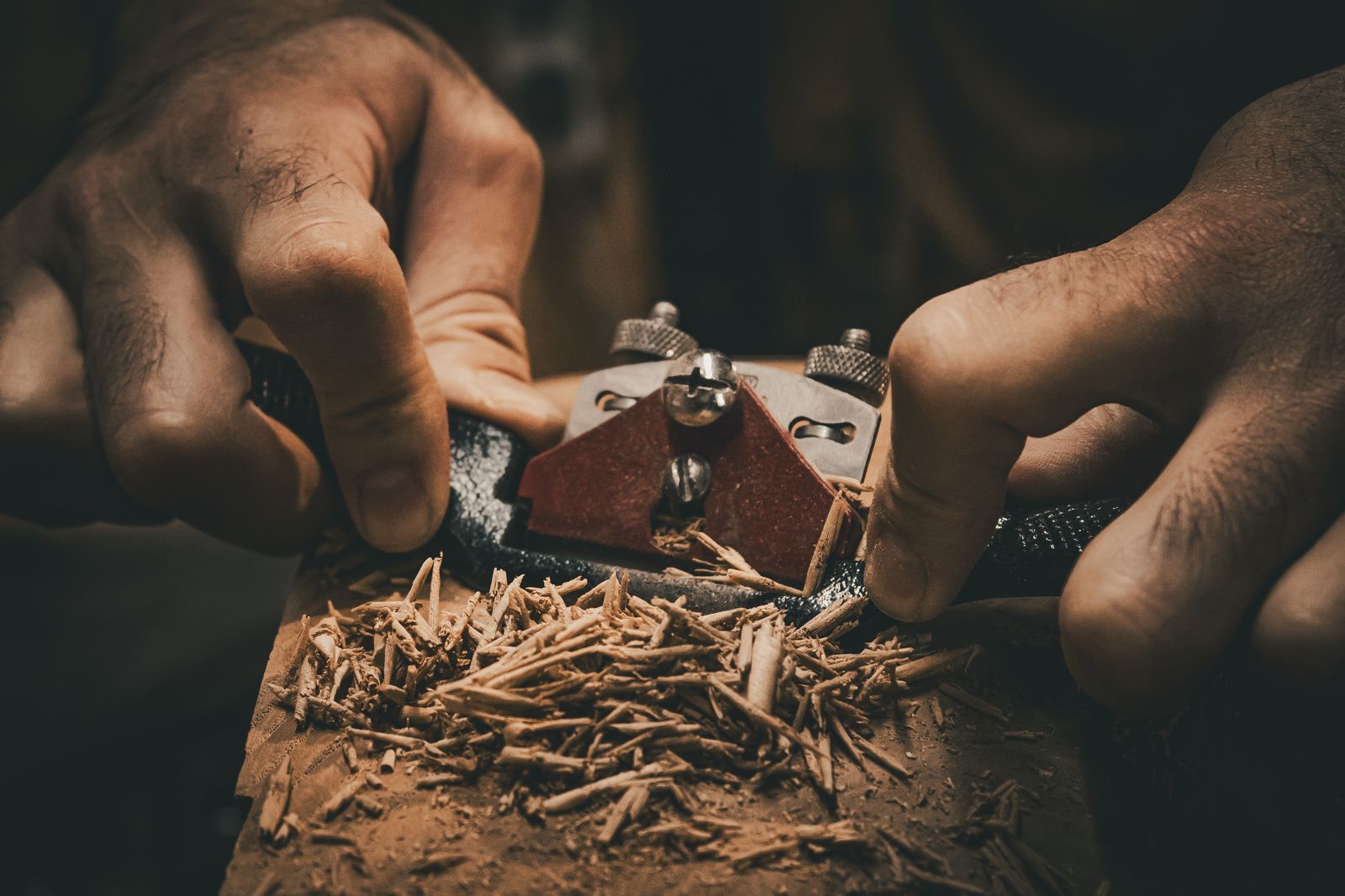 Detailed view of hands using a hand plane tool in woodworking, creating wood shavings.