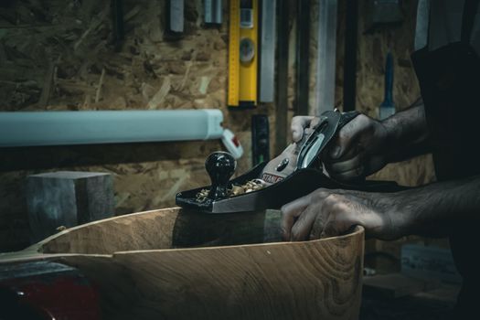 Close-up of craftsman smoothing wood with a hand plane in a workshop, emphasizing skilled carpentry.