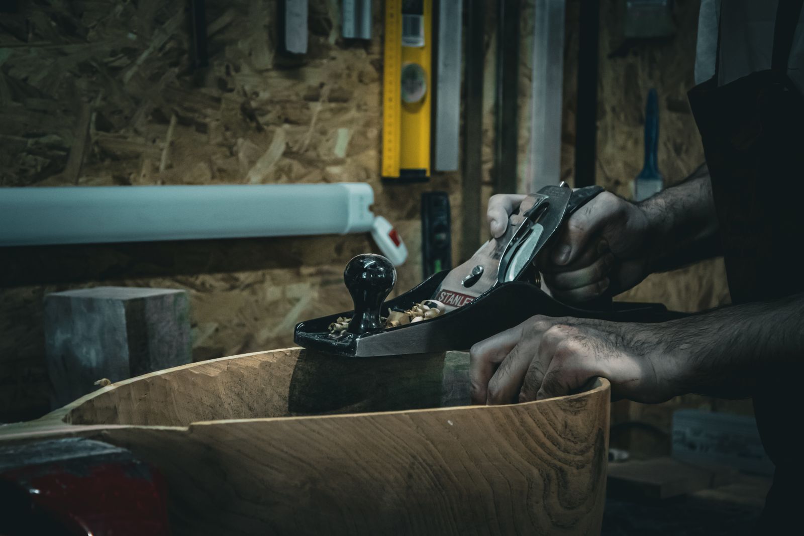 Close-up of craftsman smoothing wood with a hand plane in a workshop, emphasizing skilled carpentry.