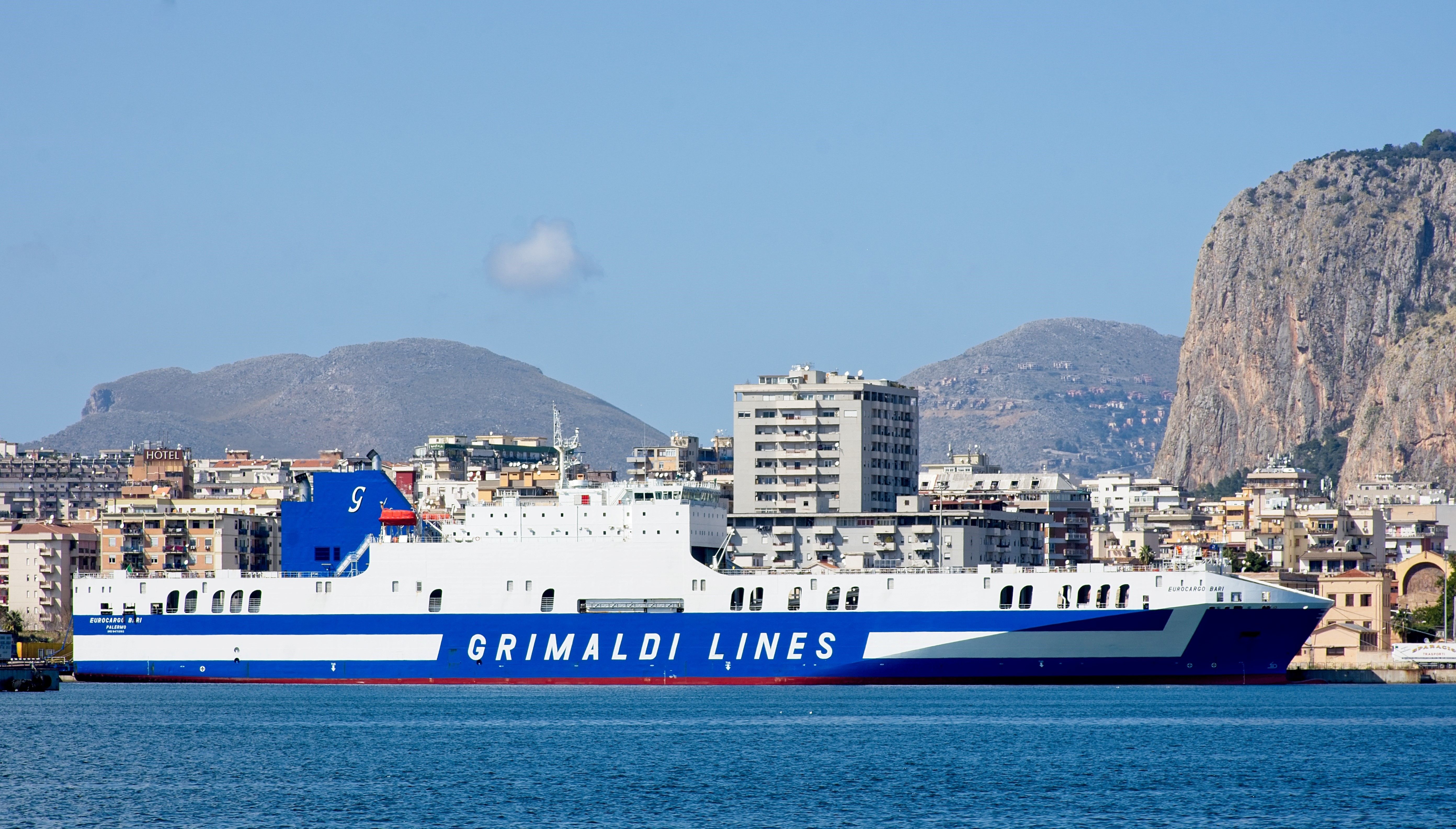 Palermo harbor at dusk with ferry and port infrastructure, warm evening light over the water and city silhouette in the background