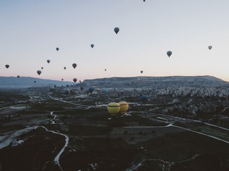 Scenic view of numerous hot air balloons rising over the landscapes of Cappadocia at sunrise.