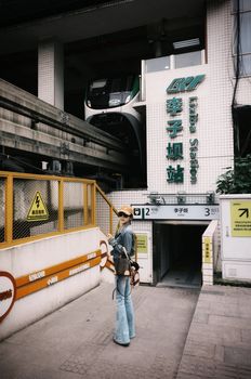 Stylish woman standing at Liziba Station, Chongqing, with a monorail in background.