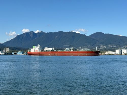 Free A large cargo ship sailing in Vancouver Harbor against scenic mountain backdrop. Stock Photo