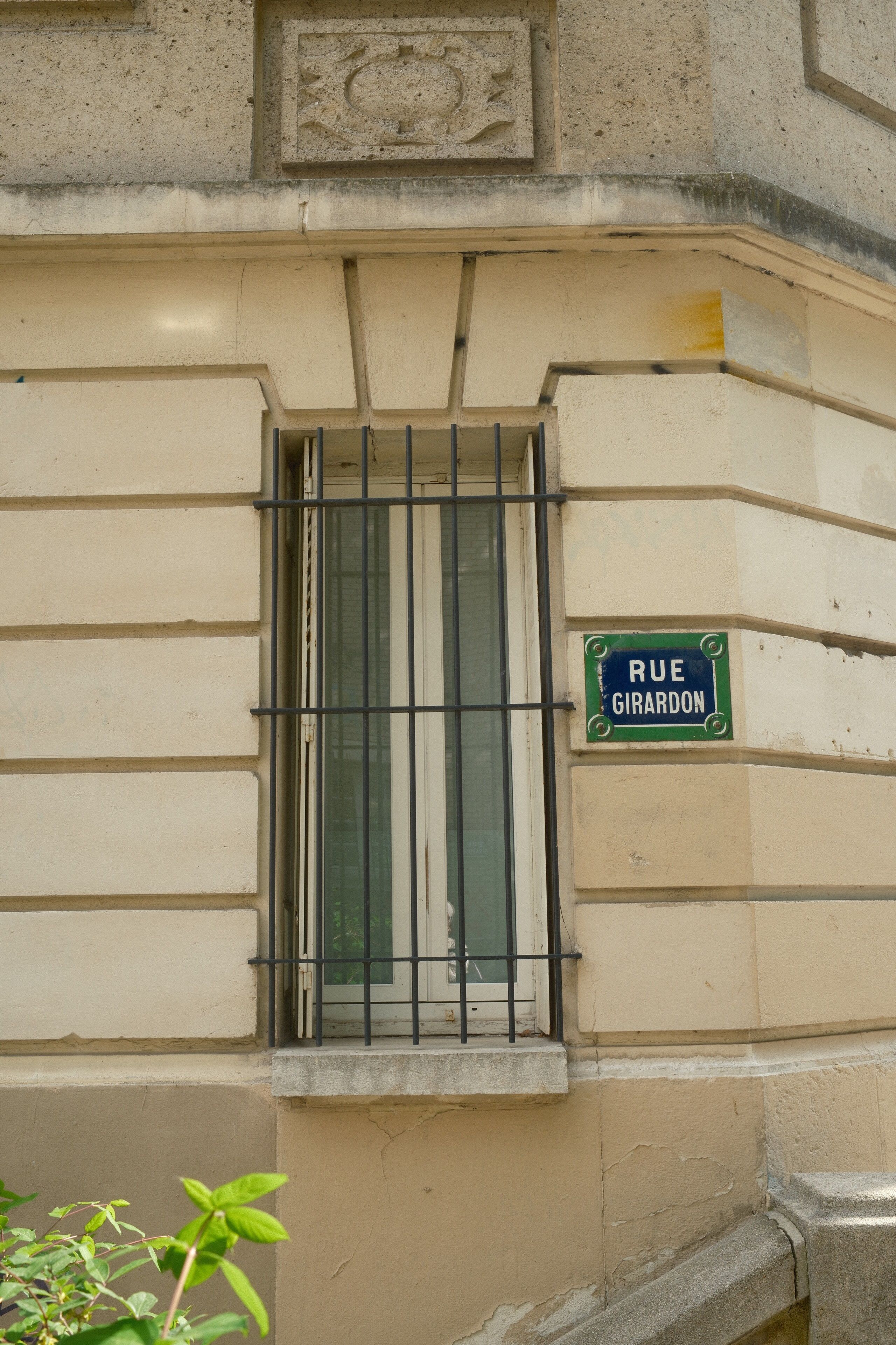 Sunny day view of a window on Rue Girardon, Paris with classic architectural details.