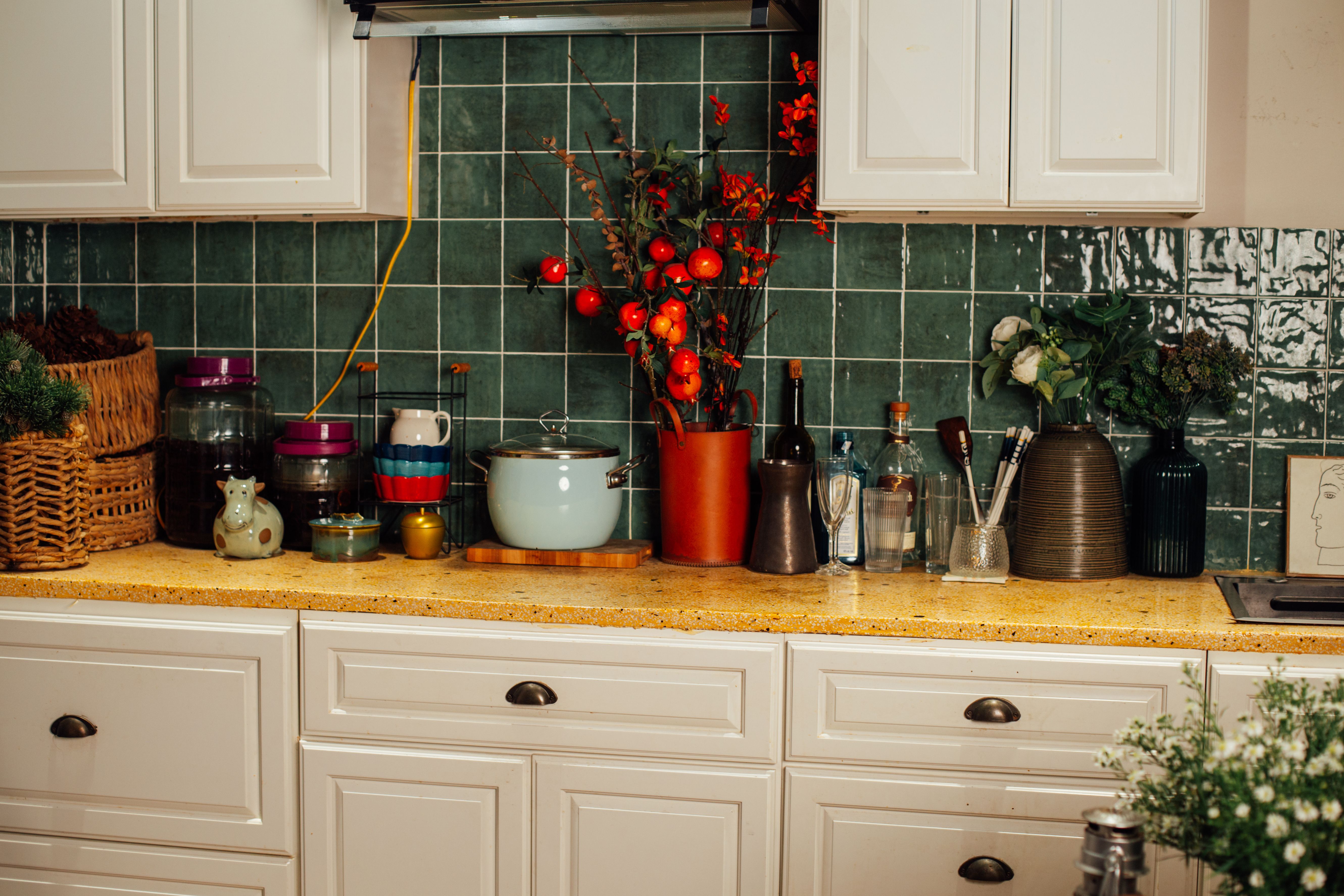 A charming kitchen counter featuring decorative items and utensils against a green tile backsplash.