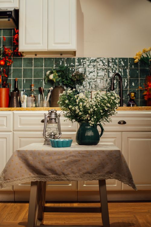 Free Cozy kitchen with a table featuring a green vase and white flowers, creating a homey atmosphere. Stock Photo