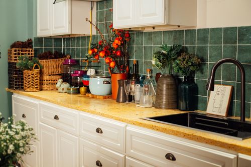 Free A charming kitchen countertop adorned with flowers, vases, and wicker baskets against vibrant green tiles. Stock Photo