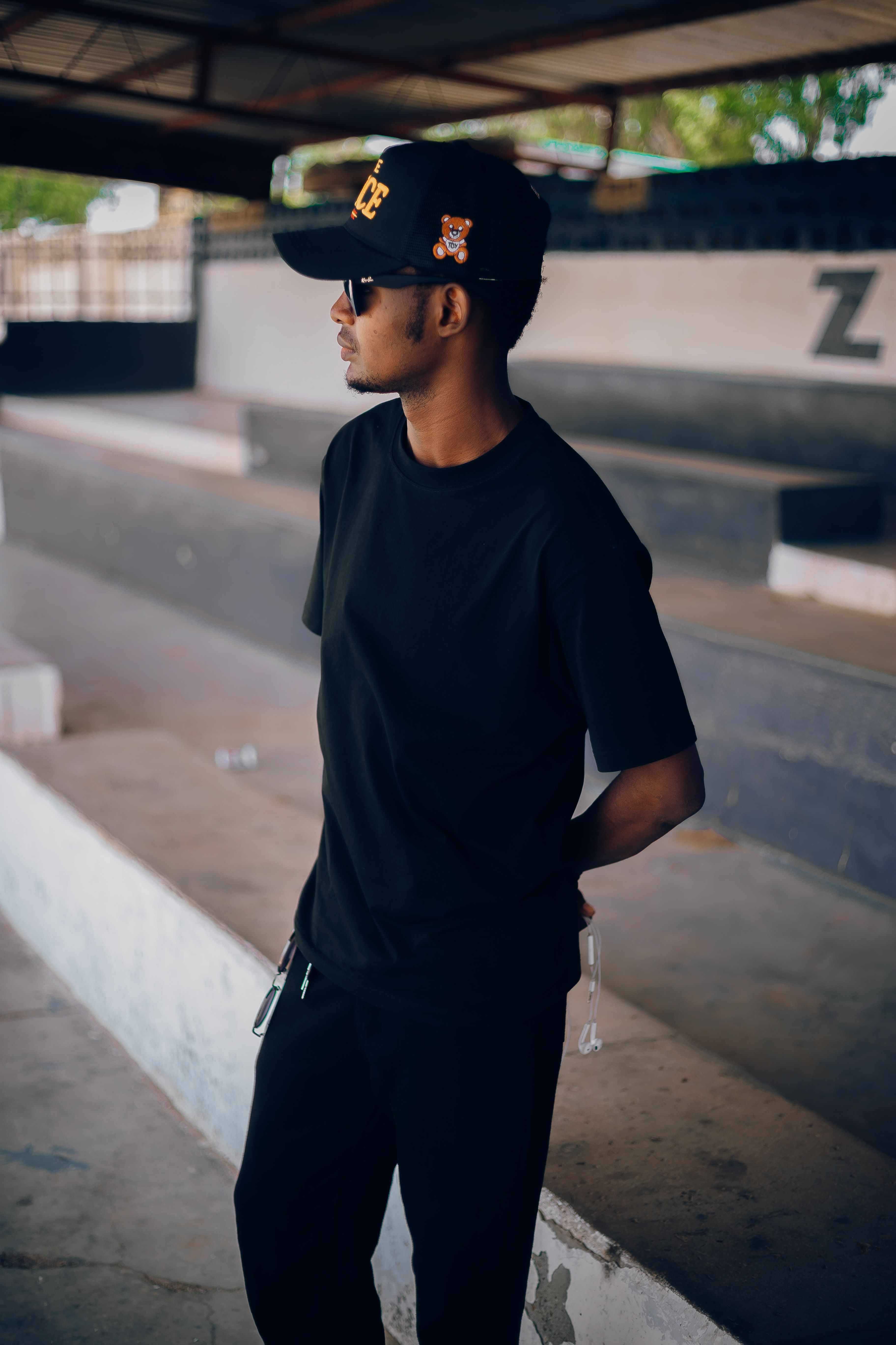Stylish young man in black attire stands in a sunny stadium in Nigeria, looking confident.