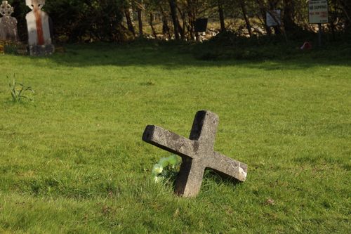Free A leaning stone cross in a serene cemetery setting under a sunny sky, signifying tranquility and heritage. Stock Photo