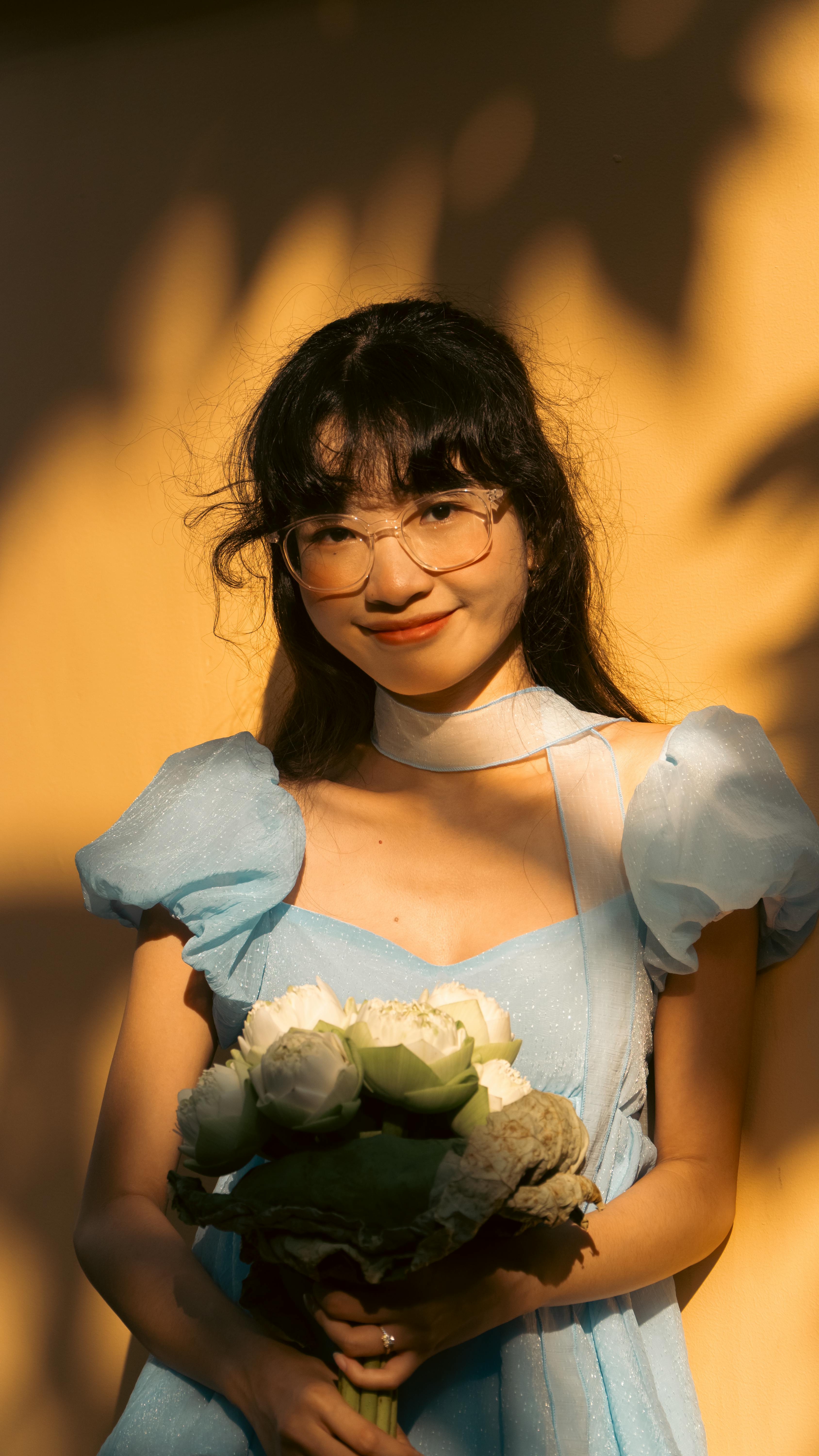 Smiling woman in blue dress with flowers, lit by warm sunlight.