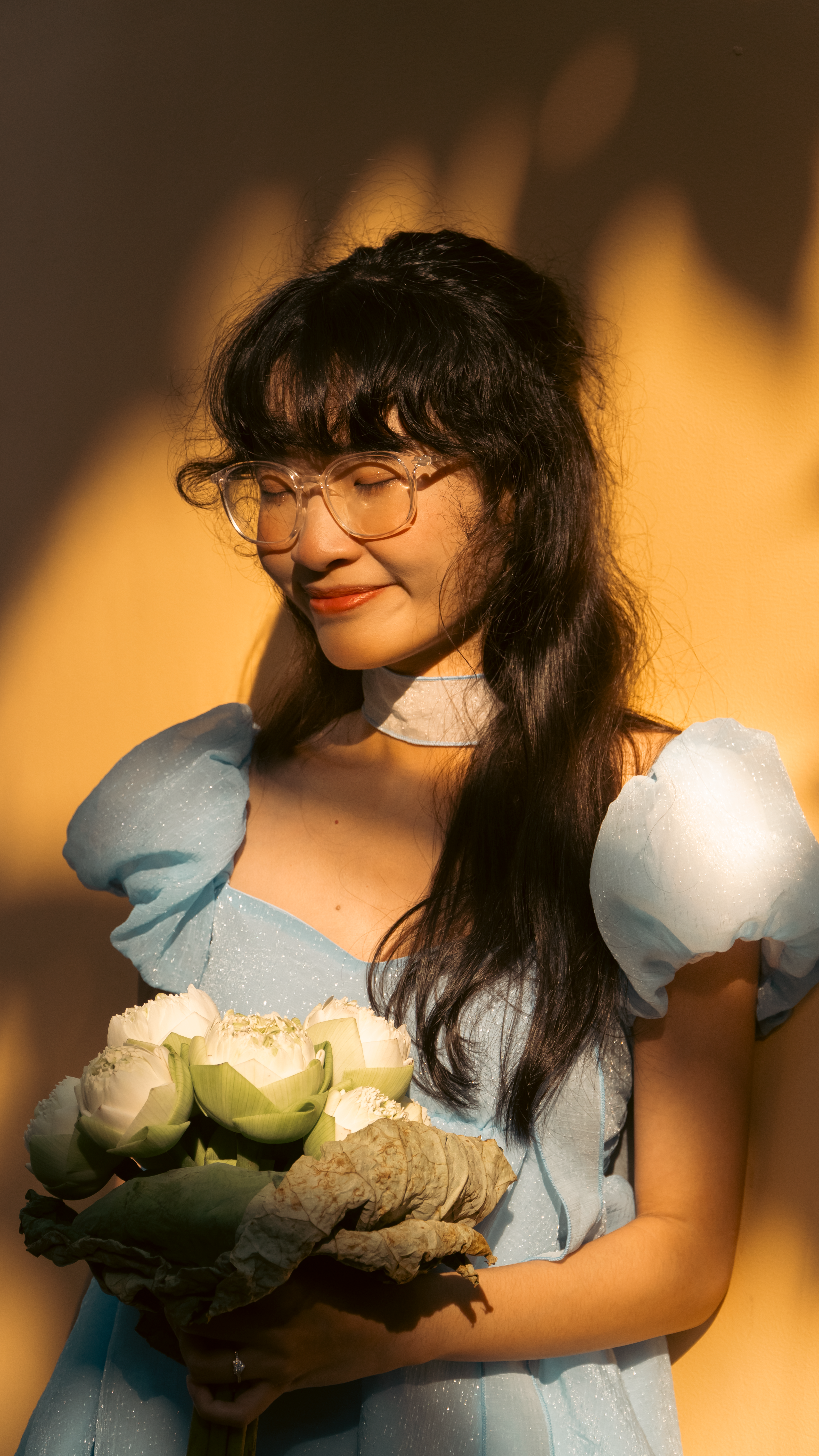 Young woman in a blue dress holding white roses with a warm, sunny glow.