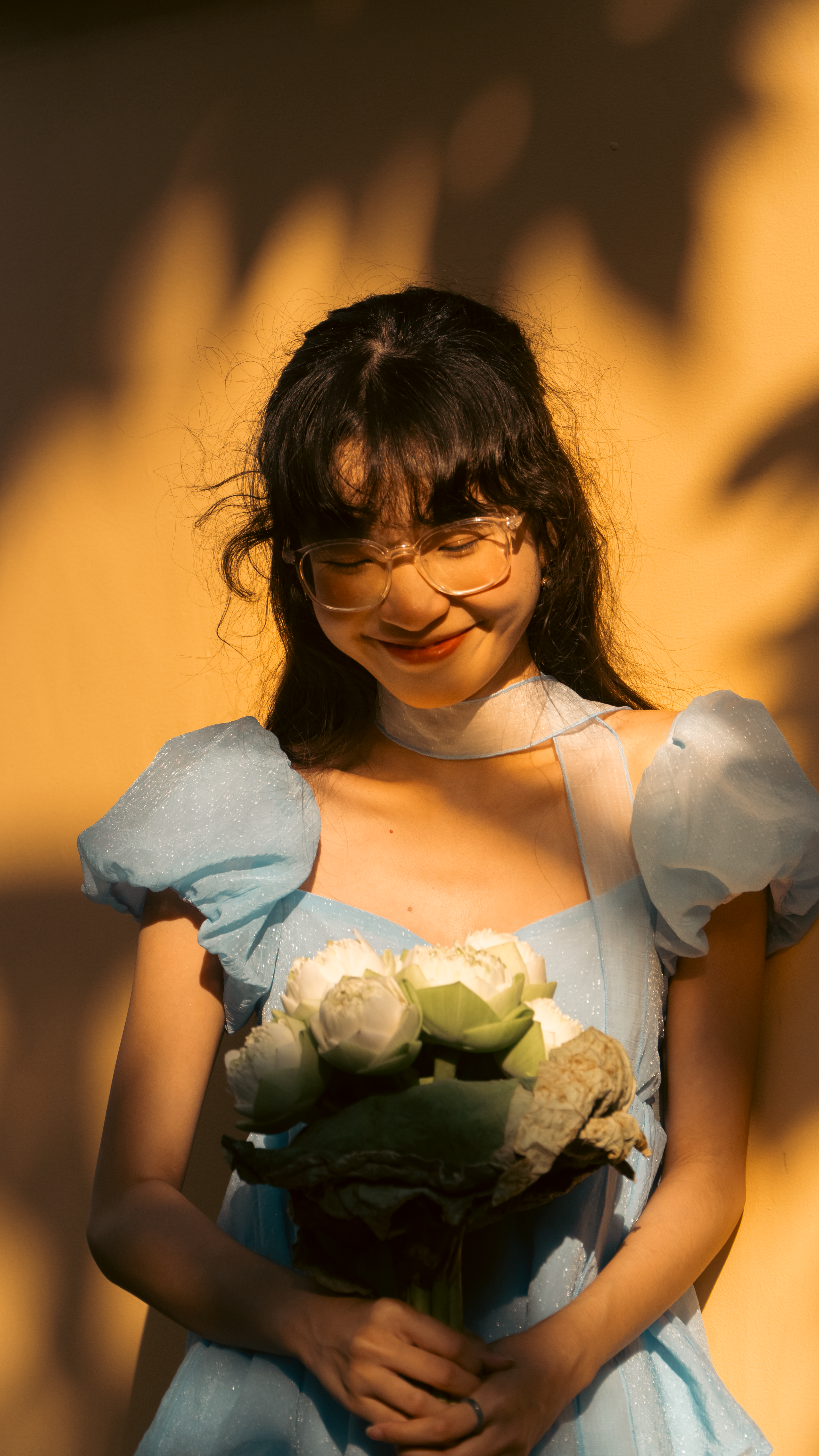 Young woman in a blue dress holding a bouquet of light green lotus flowers.