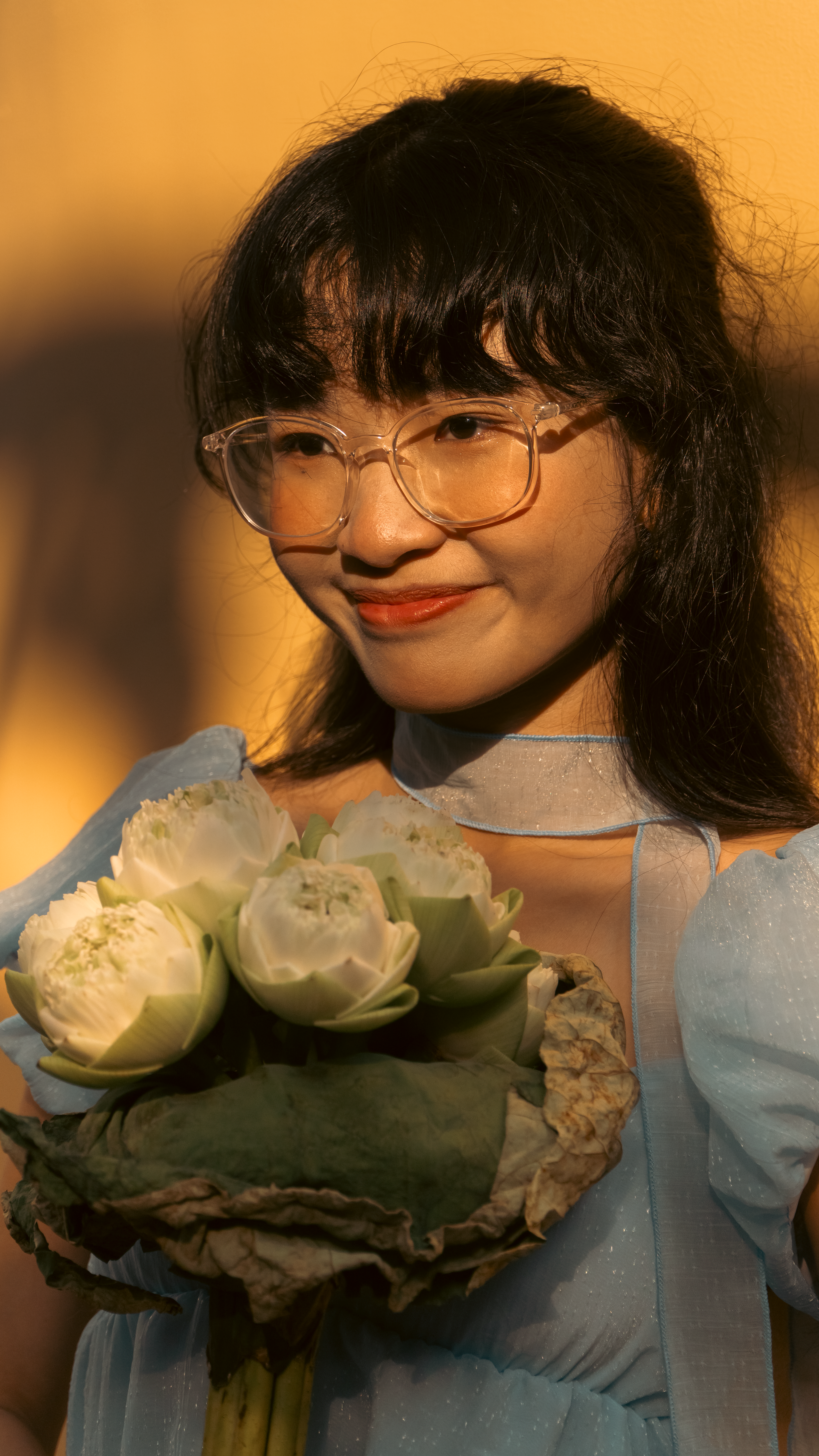Woman smiling while holding a bouquet of white lotus flowers outdoors in warm sunlight.