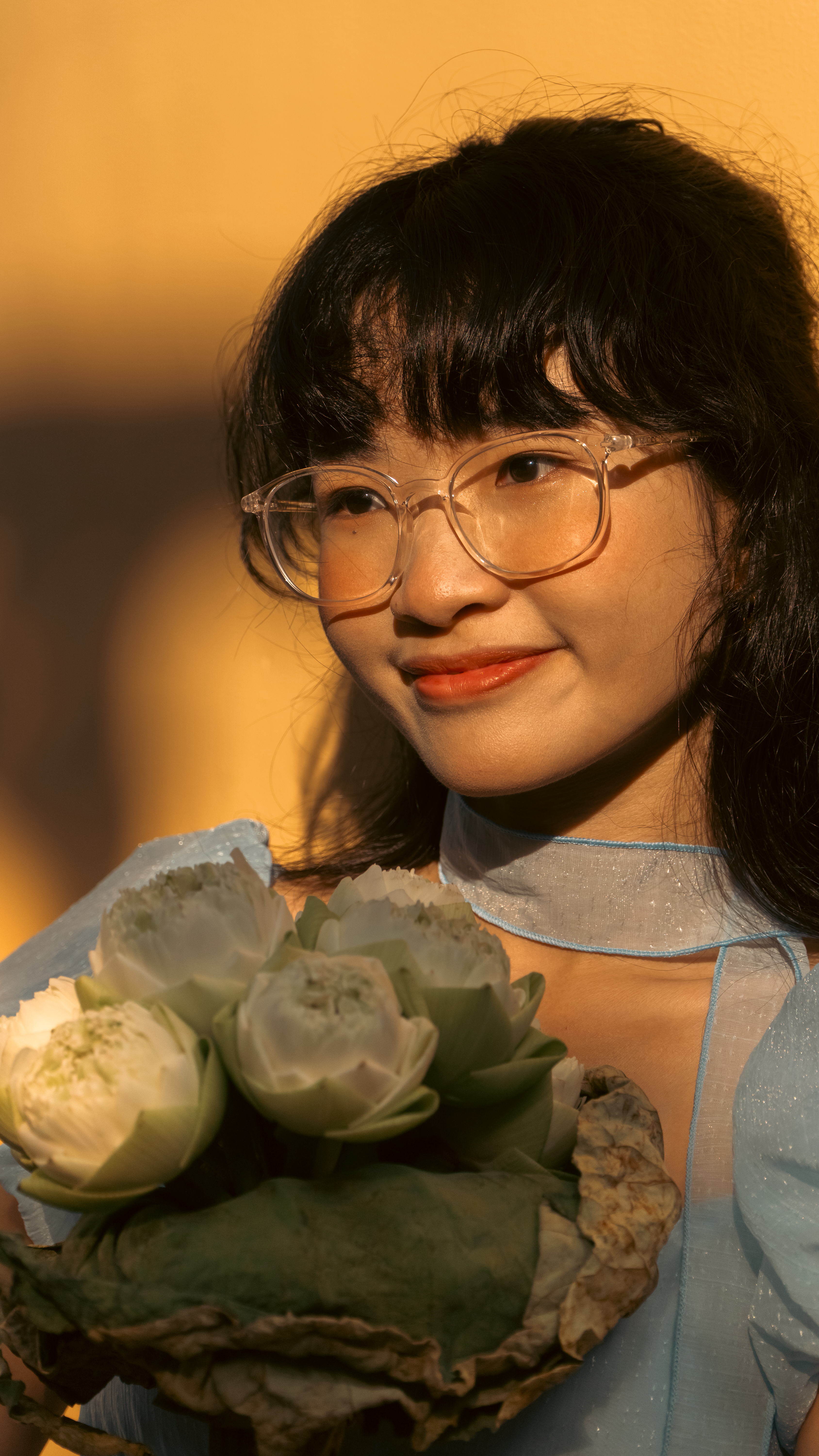 A smiling woman in glasses holding white flowers in soft, warm sunlight.