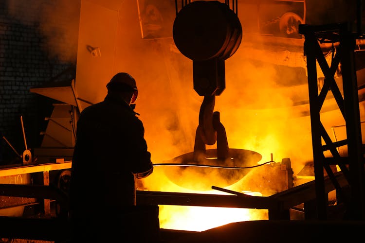 Silhouette Of Man In Helmet Standing Near Steel Melting Pool