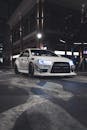 一辆时尚的白色跑车，前灯明亮，停在夜晚光线昏暗的城市街道上