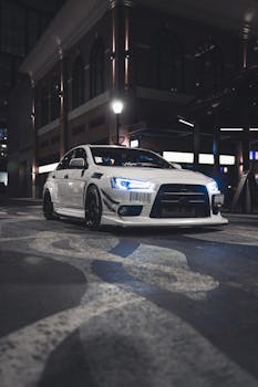 一辆时尚的白色跑车，前灯明亮，停在夜晚光线昏暗的城市街道上