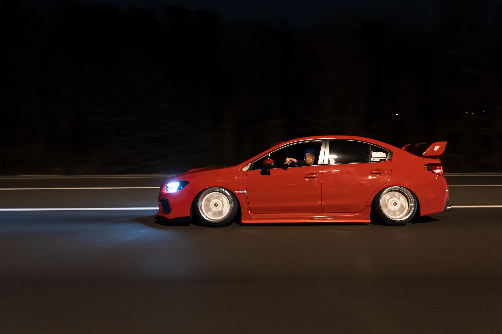 Sleek red sports car driving fast on a highway at night with motion blur.
