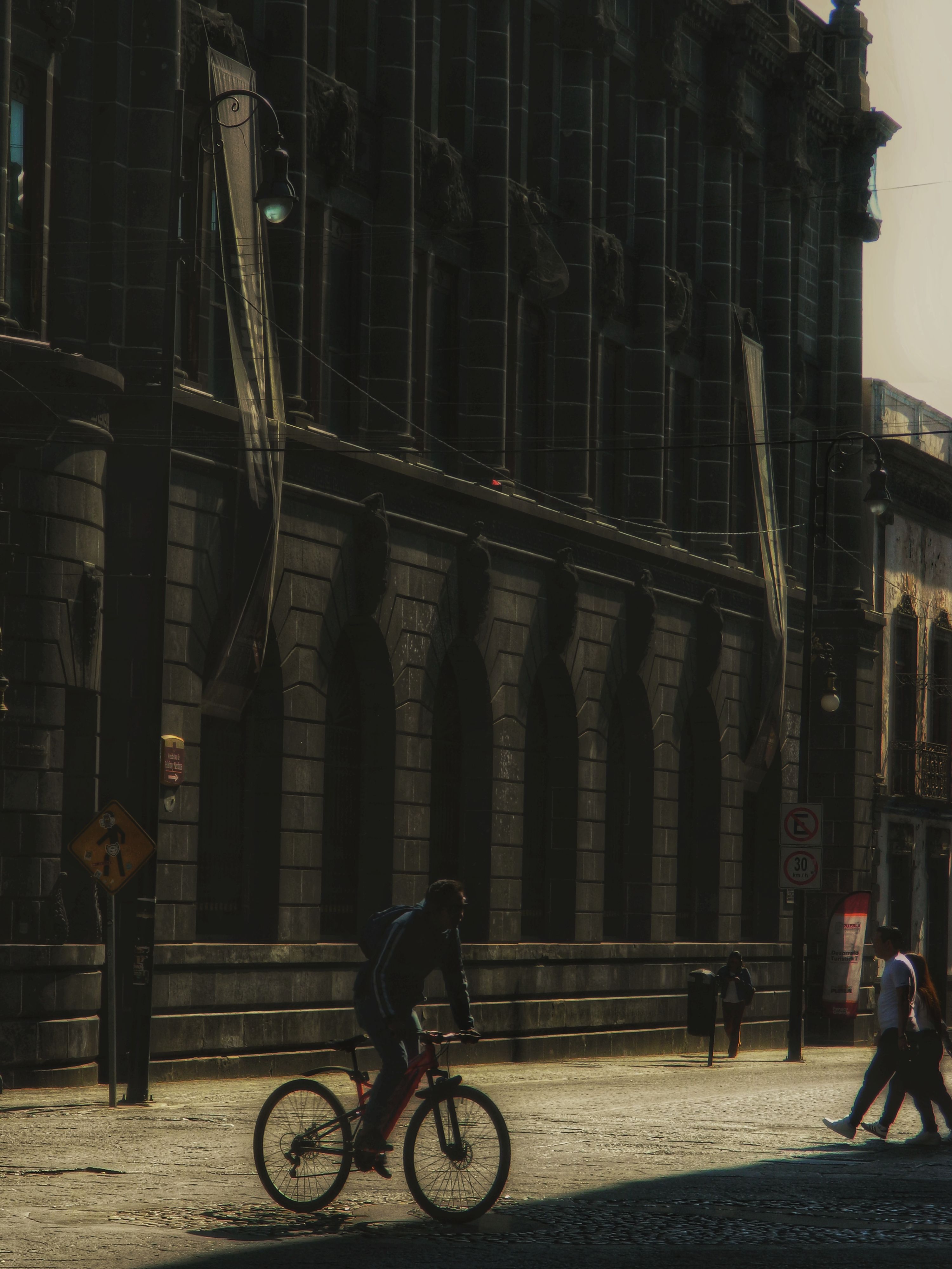 A cyclist and pedestrians against a historic urban building in soft light.