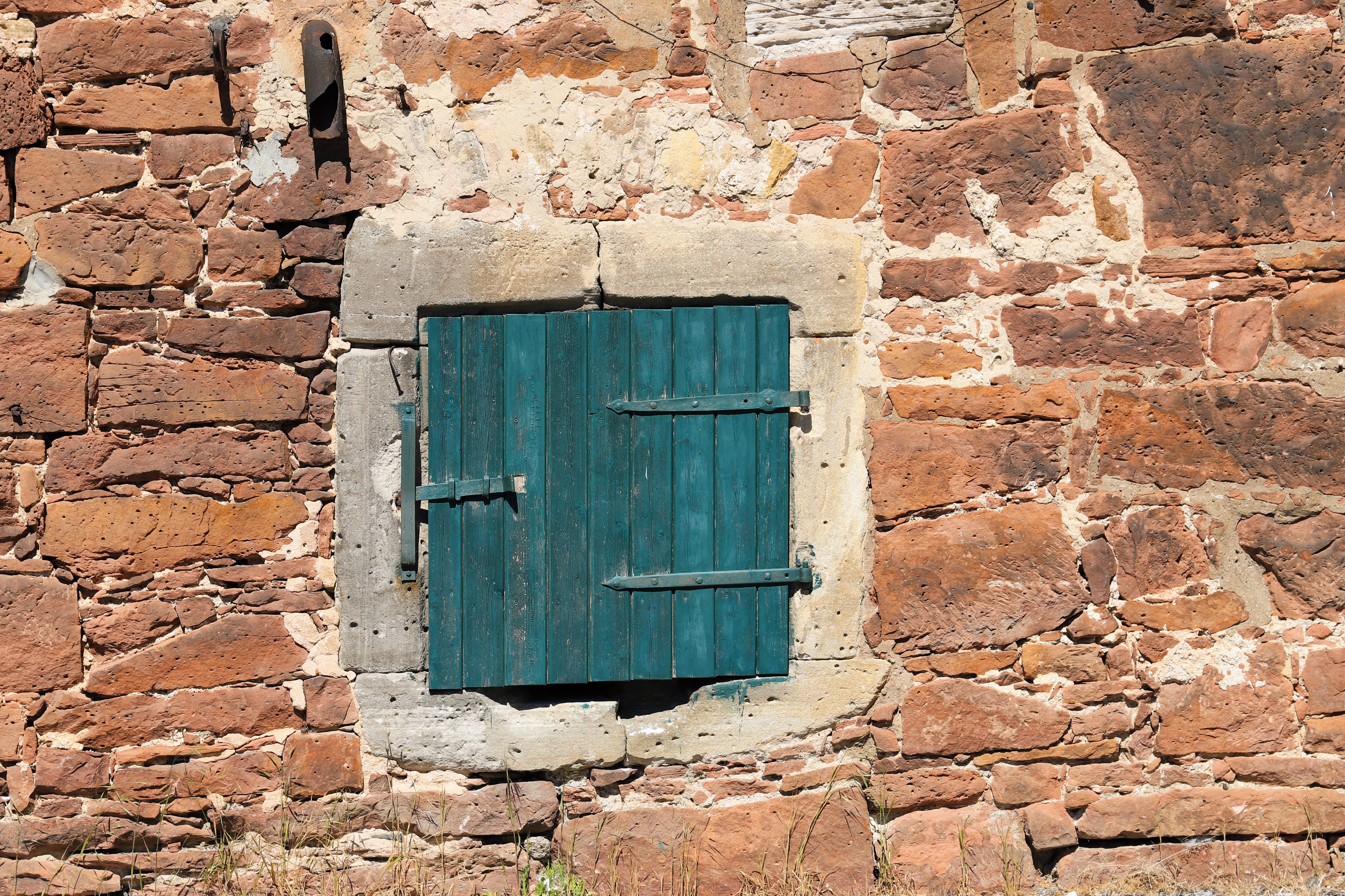 Vintage stone wall with a blue wooden shuttered window, showcasing rustic architecture and texture.