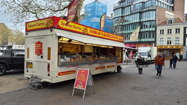 A colorful street food truck in Utrecht selling churros and oliebollen in a lively city square.