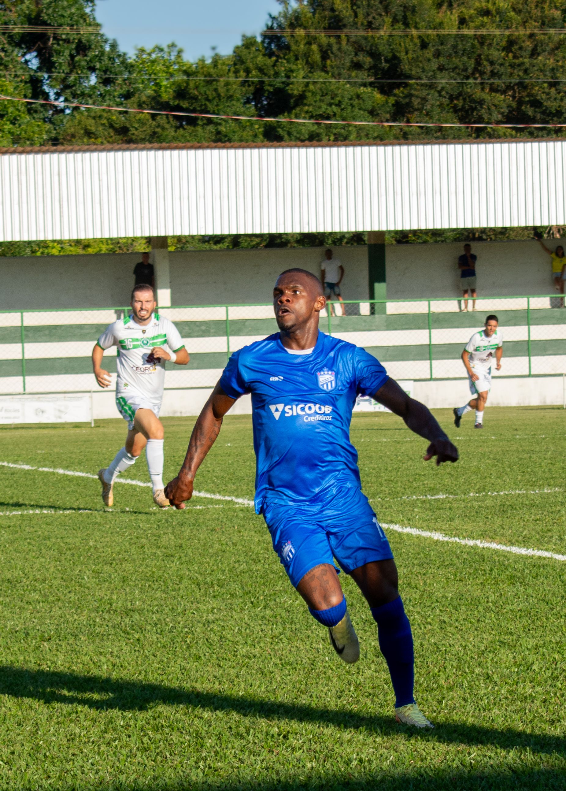 Soccer players in action during an outdoor match on a sunlit green field.