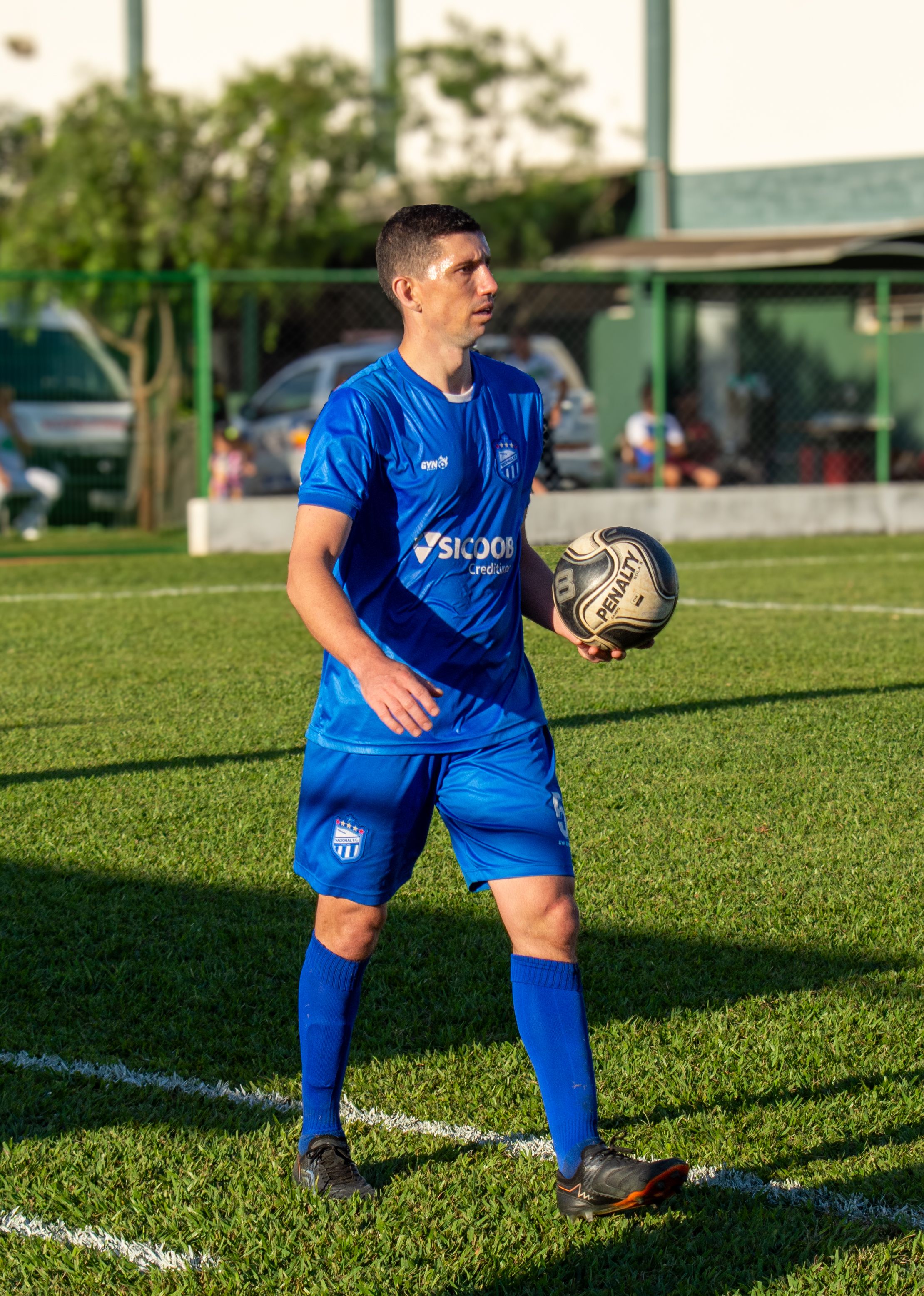 A soccer player in blue uniform holding a ball, ready for a throw-in on a sunny day.