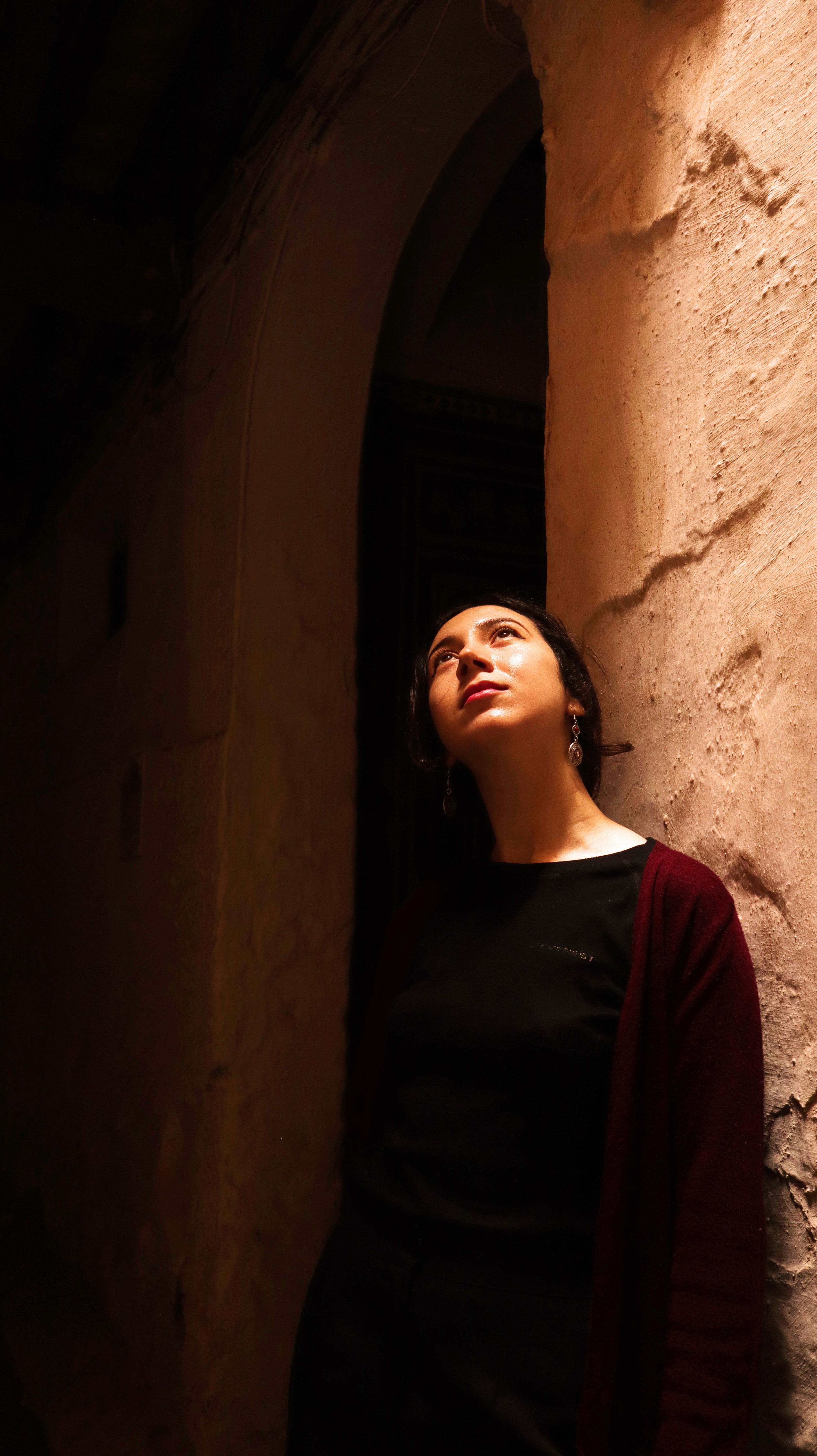 A woman gazes upwards in a narrow, dimly lit alleyway in Tetouan, Morocco.