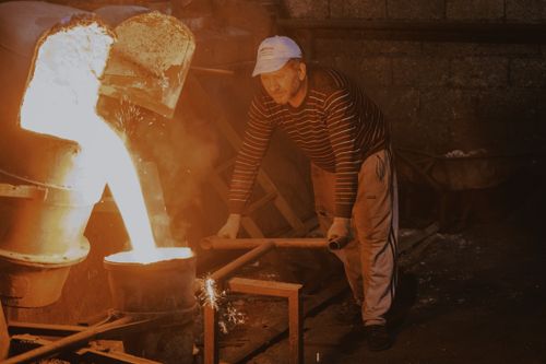 Free Male worker pours molten metal in a foundry setting, showcasing industrial work. Stock Photo