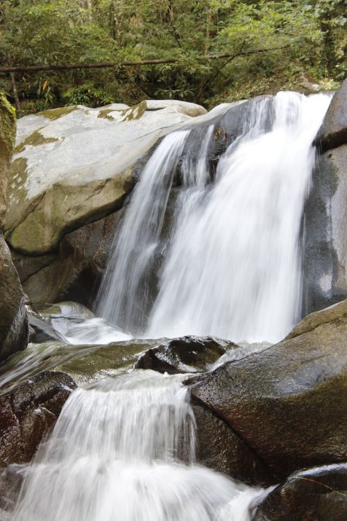 Free Beautiful waterfall flowing over rocky terrain amidst lush greenery. Stock Photo