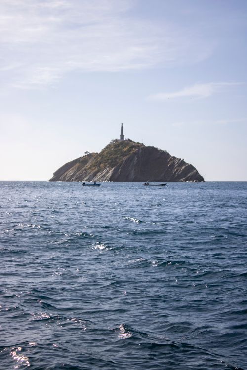 Free Scenic view of an island with a lighthouse surrounded by calm ocean waters. Stock Photo