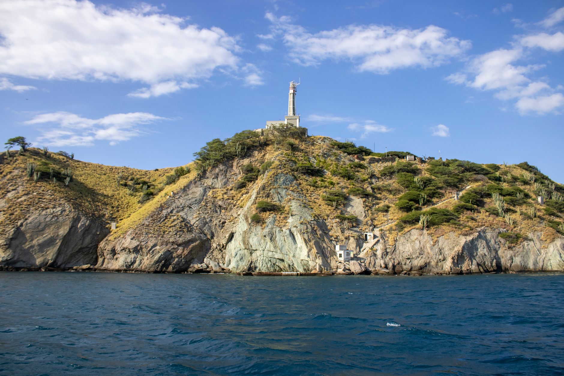 A picturesque coastal hill with a lighthouse under a bright blue sky and gentle sea.