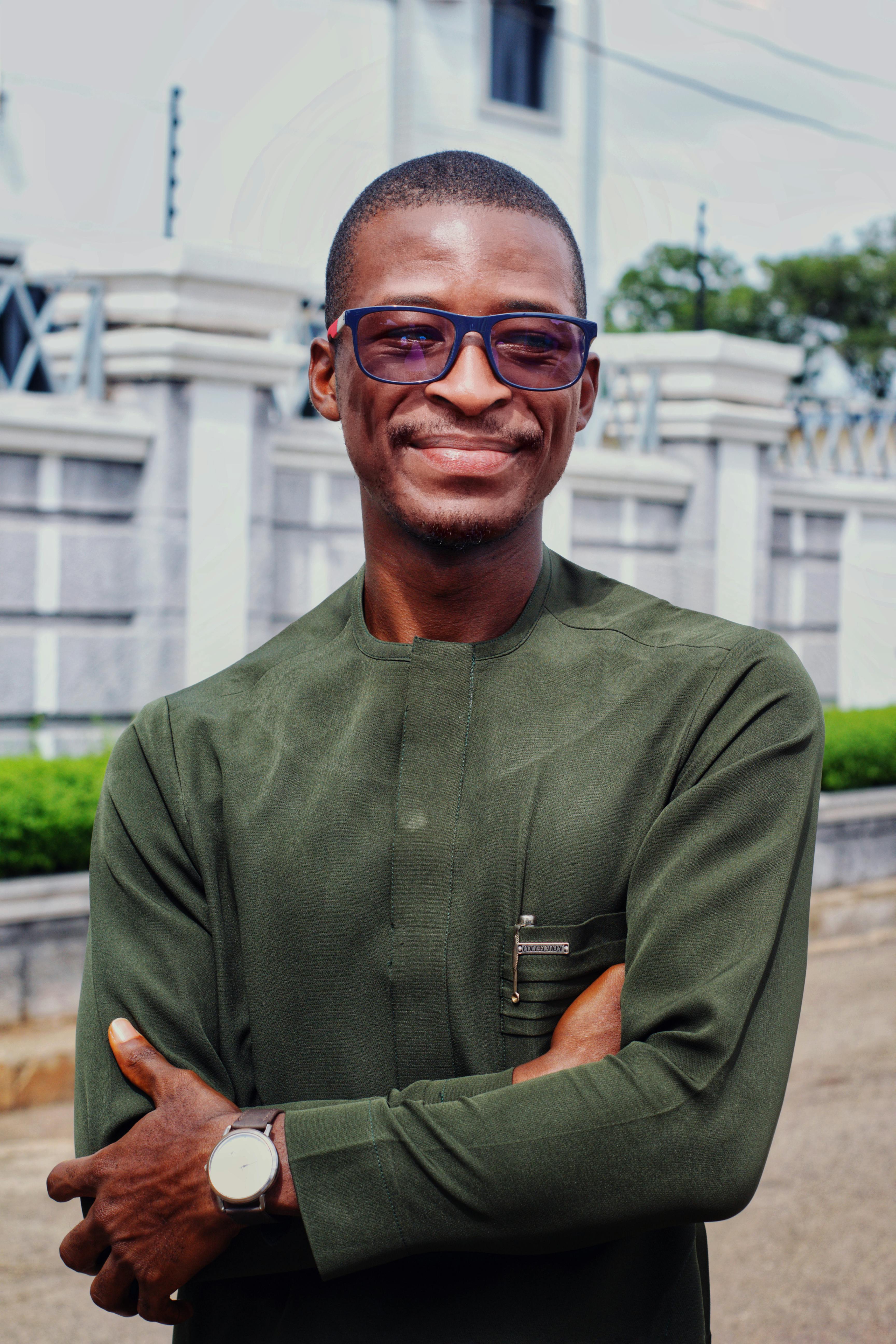 Smiling man in glasses and green attire posing confidently outside.