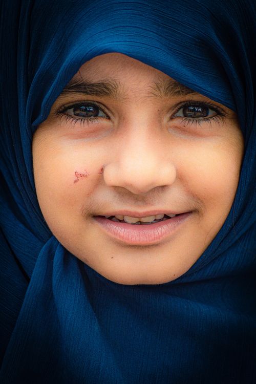Free Close-up portrait of a smiling girl in a blue hijab, exhibiting warmth and innocence. Stock Photo
