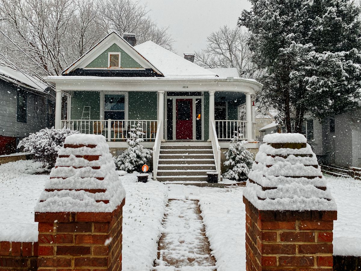 A snow-covered house with a front door entrance in winter weather conditions