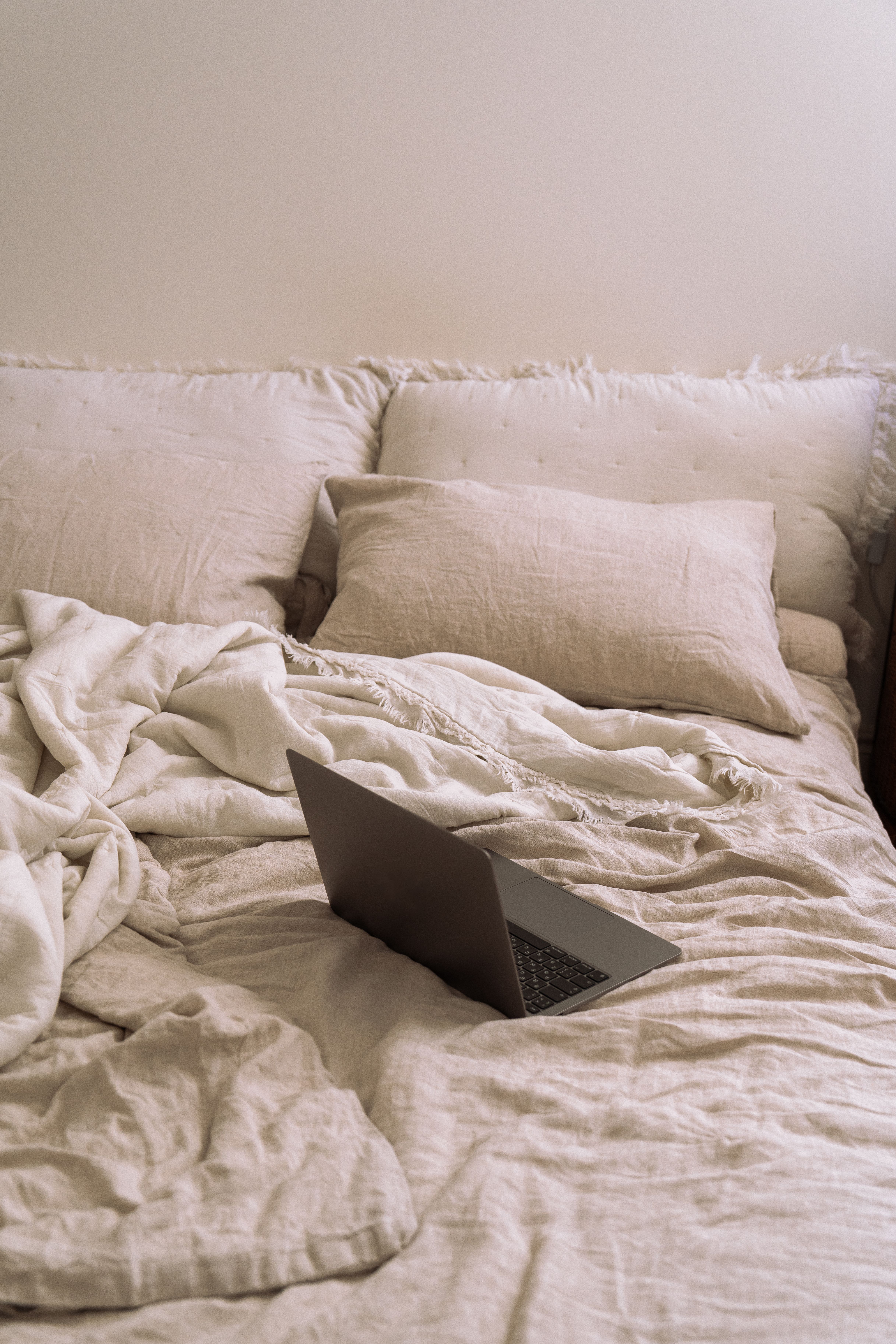 A laptop on a neatly arranged bed with soft pillows and blankets in a cozy room.