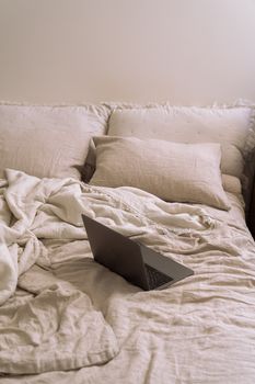A laptop on a neatly arranged bed with soft pillows and blankets in a cozy room.