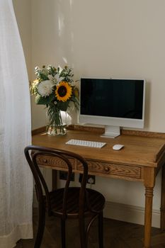 Cozy home workspace featuring a computer on a wooden desk with a bouquet of sunflowers and lilies.
