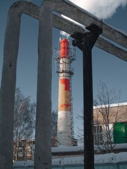 A tall industrial chimney with smoke set against a clear blue winter sky.