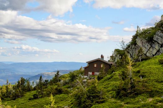 A charming wooden cabin nestled in the mountainous landscape under a bright sky.