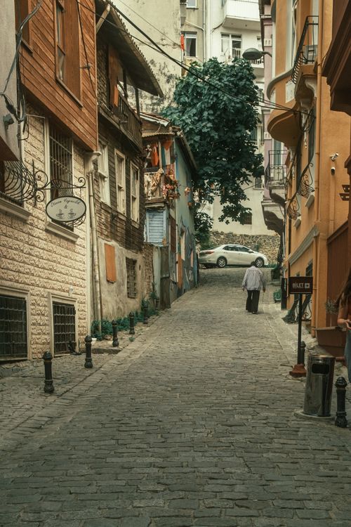 Free A picturesque cobblestone alley with colorful buildings and a single person walking in a historic city. Stock Photo