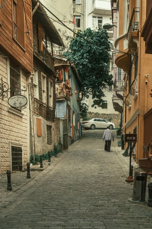 Free Quaint cobblestone street in Europe with colorful buildings and a lone pedestrian. Stock Photo