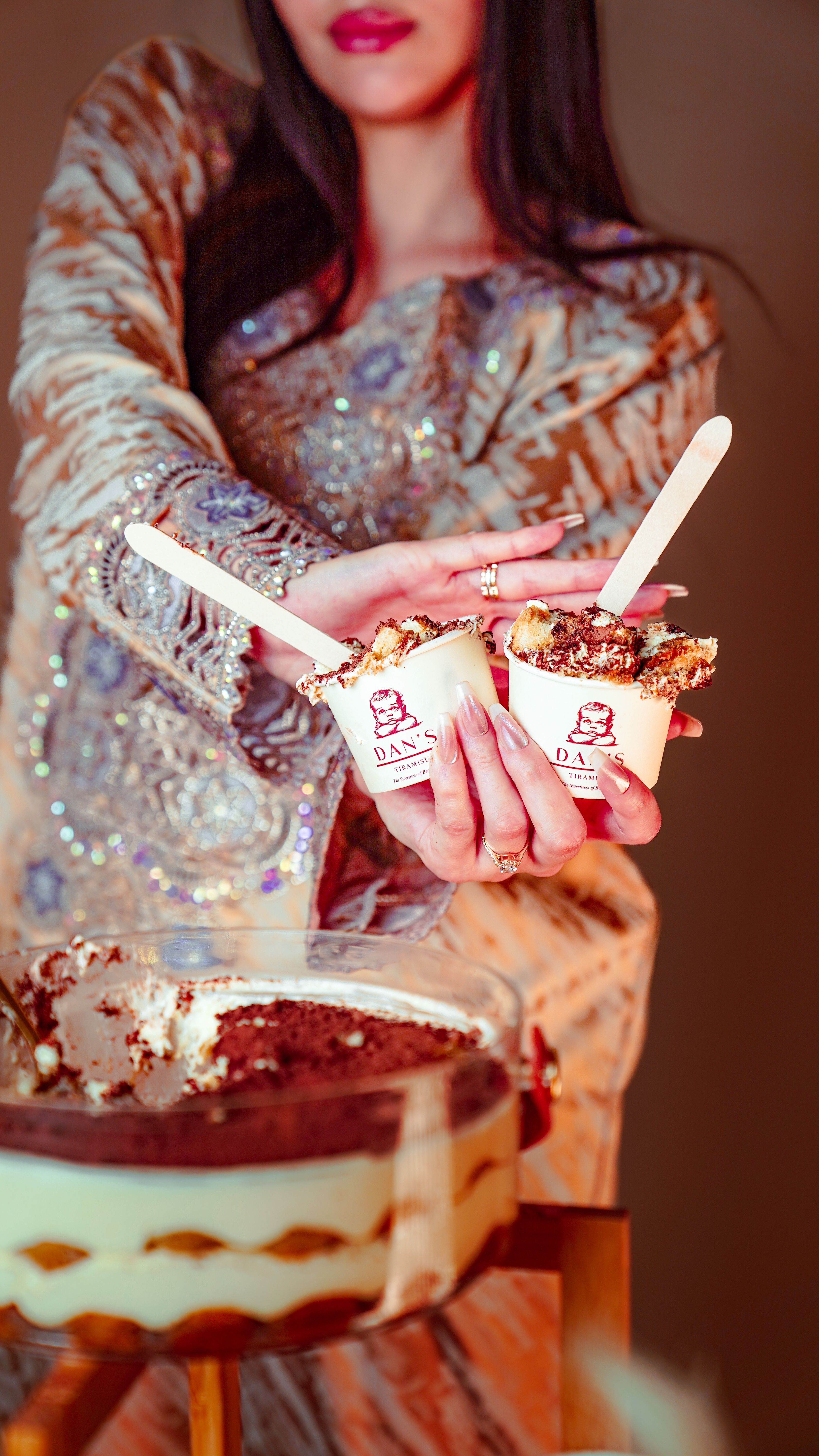 A stylish woman holding cups of tiramisu, dressed in traditional attire in the UAE.