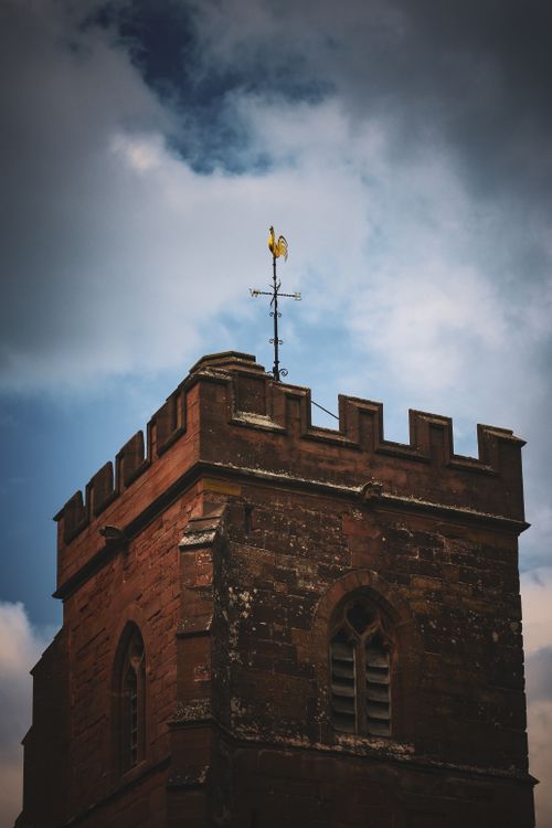 Free A historic church tower in Kinver, England, stands tall against a backdrop of a dramatic cloudy sky. Stock Photo
