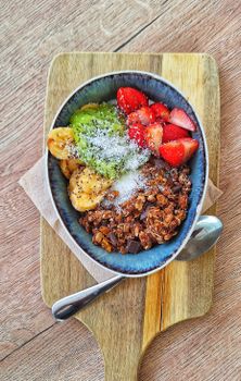 Delicious fruit and granola bowl with coconut on wooden board, perfect for a fresh start.