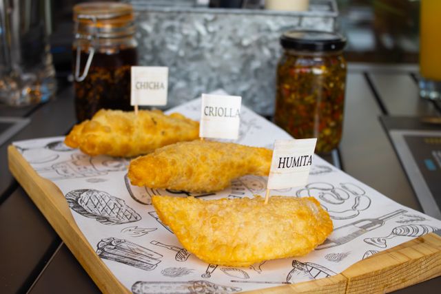 A trio of labeled empanadas served on a tray, showcasing traditional flavors like Chicha, Criolla, and Humita.