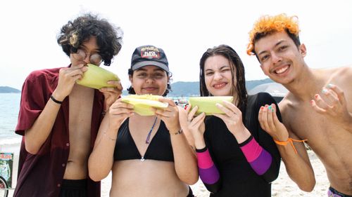 Free A group of friends savoring corn at the beach, soaking up the summer sun and fun. Stock Photo