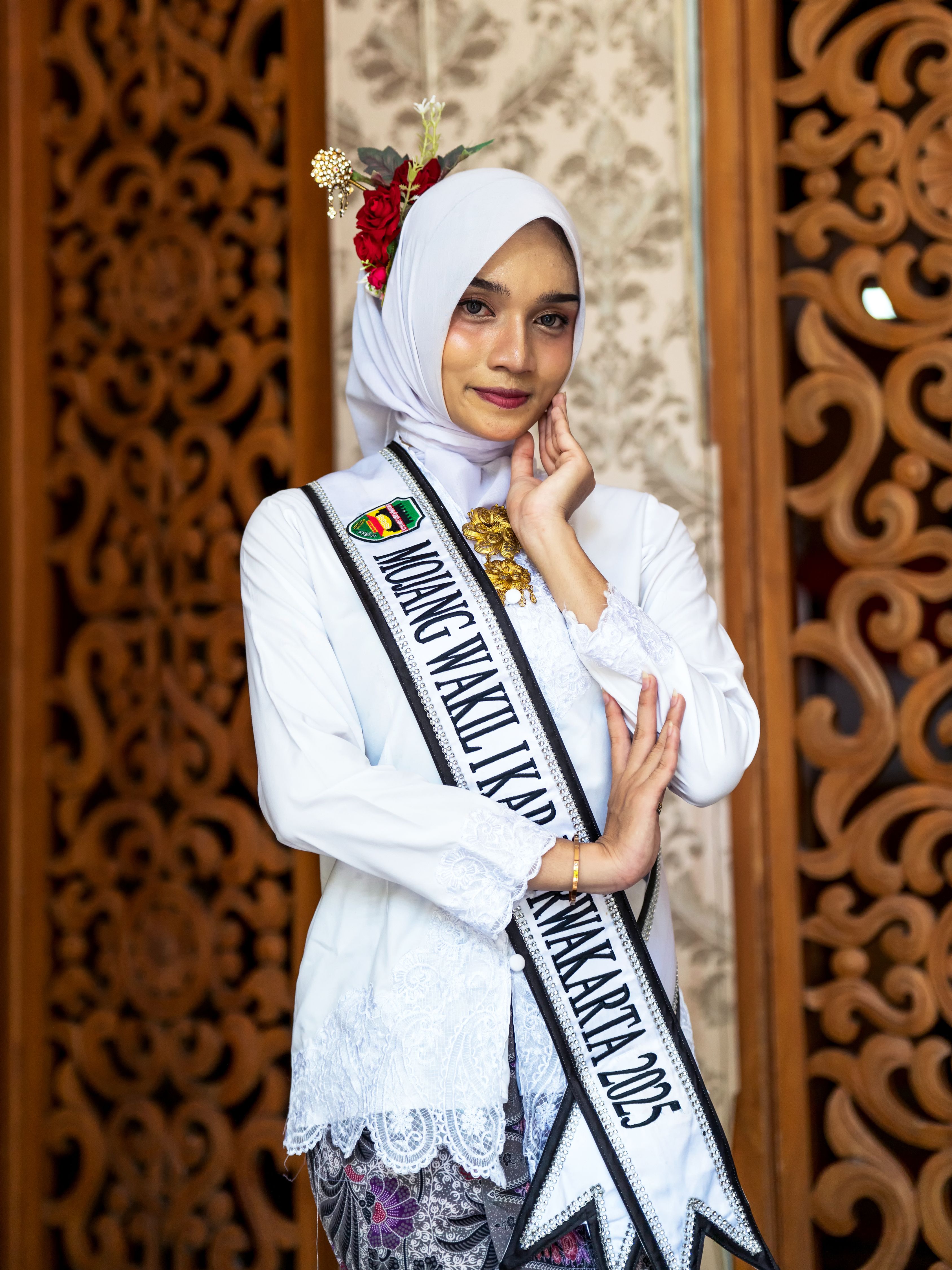 Portrait of an Indonesian pageant contestant in traditional attire with hijab and sash indoors.